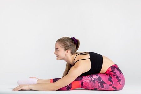 Full length portrait of a young sportwoman stretching muscles while sitting on the floor isolated...