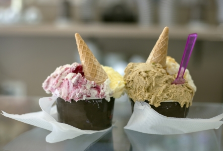 Two portions of delicious ice cream in paper cups topped with syrup and waffle cones 