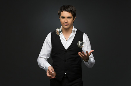 Handsome young man dressed in suit juggling three glass balls over black backgroundの写真素材