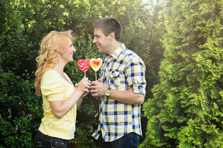 Beautiful couple holding heart shaped red and yellow lollipopsの写真素材