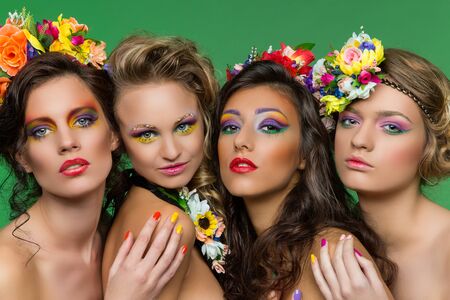 Portrait of four young beautiful girls wearing flower accessories over green backgroundの写真素材