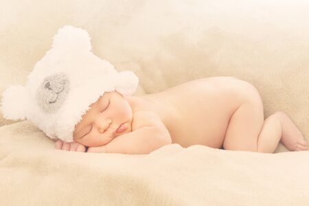 Portrait of  newborn baby boy wearing funny bear shape hat sleeping on soft beige coverの写真素材