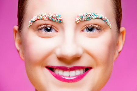 Closeup portrait of smiling beautiful girl with colorful small candies on her eyebrowsの写真素材