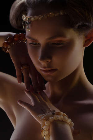 Young beautiful girl wearing bijou in dark light over black backgroundの写真素材
