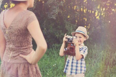 Outside shot of little boy taking picture of older girl using retro film cameraの写真素材