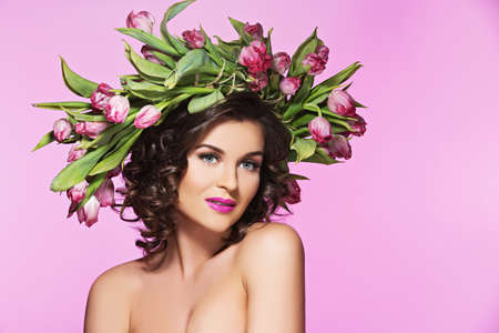 Attractive young woman with bright make-up and flowers on her head over pink backgroundの写真素材