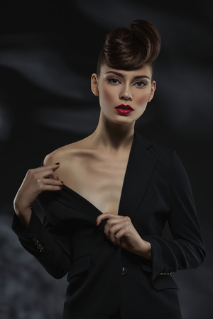 Beautiful young woman wearing black jacket showing her shoulder over black backgroundの写真素材