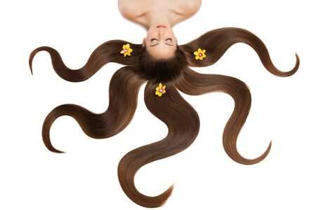 Beautiful young woman with very long natural hair and flowers on it lying on back. Isolated over white background.の写真素材