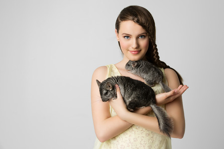 Beautiful teenage girl holding two pet chinchillas. Over light grey background.の写真素材