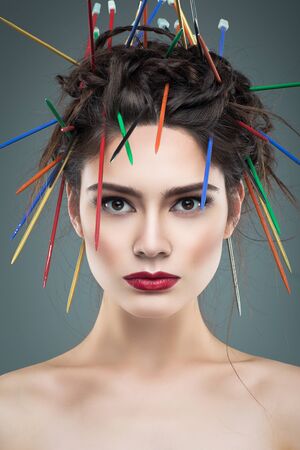 Beautiful fancy young woman with creative haitsyle. Many multicolored knitted needles in hair. Over...