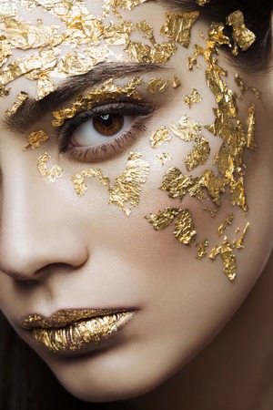 Closeup portrait of beautiful young woman with golden foil on face and lips. Creative makeup. Long hairの写真素材