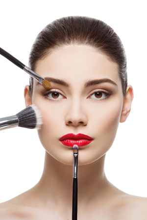 Closeup portrait of beautiful young woman with makeup brushes. Red lips. Isolated over white background.の写真素材