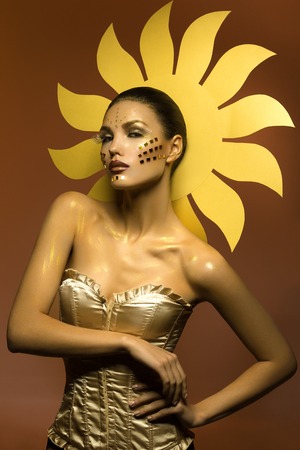 Beautiful young woman dressed as sun girl. Creative styling. Bright flame background. Copy space.の写真素材