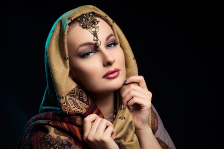 Beautiful young woman with bright makeup and shawl on head. Closeup portrait.の写真素材
