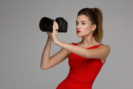 Beautiful photographer woman holding dslr camera with portrait lense. Over grey background. Copy space.の写真素材