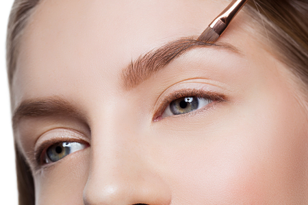 Beautician correcting eyebrows form on beautiful woman face. Beauty shot. Close-up.の写真素材