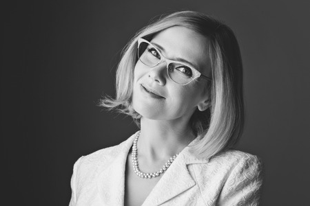 Closeup of elderly business woman in glasses. Happy smiling expression. Over grey background. Monochrome.の写真素材