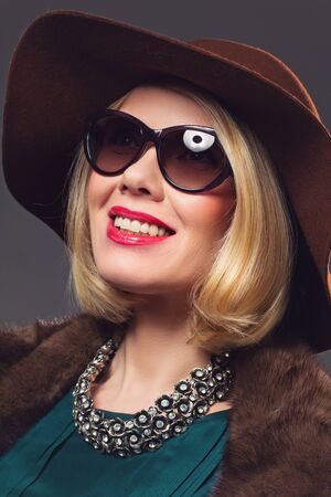 Portrait of beautiful middle aged blond woman in fur coat, sunglasses and hat. Studio shot. Over...