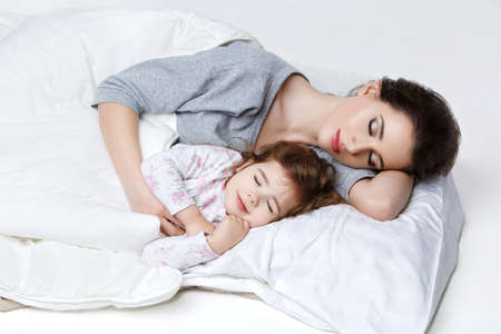 Beautiful young woman and little girl in bed. Mother and daughter.の写真素材