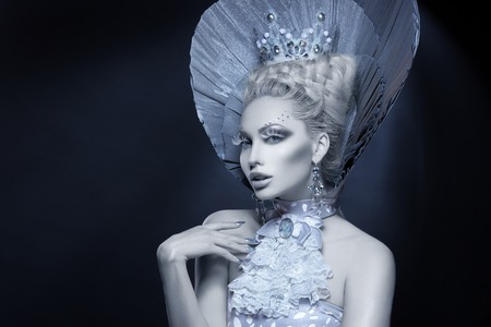 Portrait of beautiful young woman dressed as winter queen. Creative makeup. Over dark background. Copy space.の写真素材