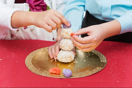 Children making christmas cake pop dessert in shape of snowman on red table