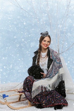 Beautiful young woman in traditional Russian clothes sitting on winter sleigh. Studio shot over white background.の写真素材