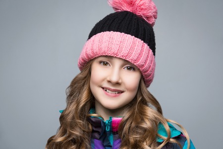 Beautiful happy teen girl with long curly hair in pink wool hat and bright warm coat. Studio shot...