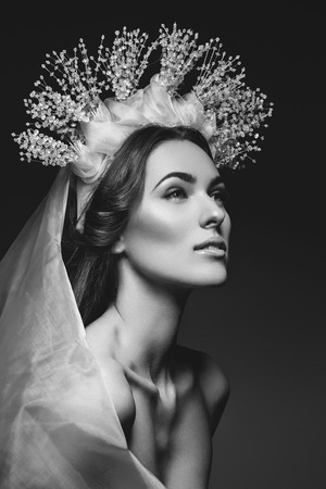 Beautiful young brunette woman in crystal crown and white veil on black background. Romantic beauty look. Copy space.の写真素材