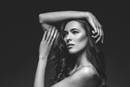 Beautiful brunette young woman with long healthy thick wavy hair and make-up on black background. Copy space. Monochrome.の写真素材