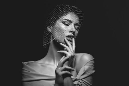 Portret of beautiful young woman with natural makeup. Face covered in veil net. Hands with beige...