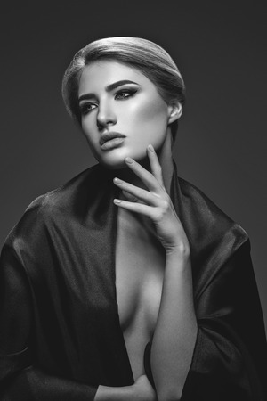 Portrait of beautiful young woman with cat eye make-up in black fabric. Studio beauty shot over black background. Monochrome.の写真素材