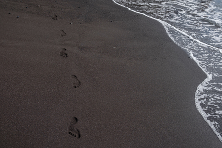 ocean water on black sandy beach. foot prints. outdoor shot on Tenerife, Spain. Copy space.の写真素材