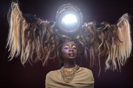 beautiful black young woman with art hair composition and gold makeup. golden goddess.  beauty studio shot on dark background. copy space.の写真素材