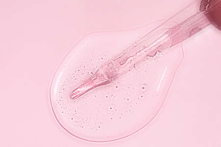 Liquid oil serum drop in pipette isolated on pastel pink background. Retinol, aha acid, collagen skincare fluid, photo with shallow depth of field. Hyaluron essence in dropper for beauty treatmentの写真素材