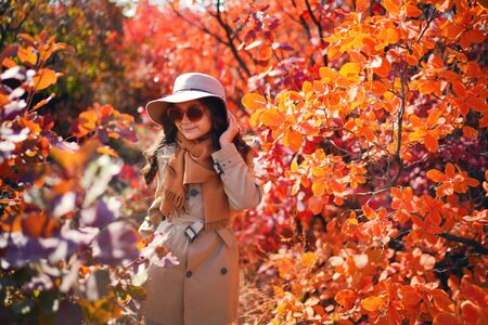 A girl in glasses, hat and coat in the autumn forest.