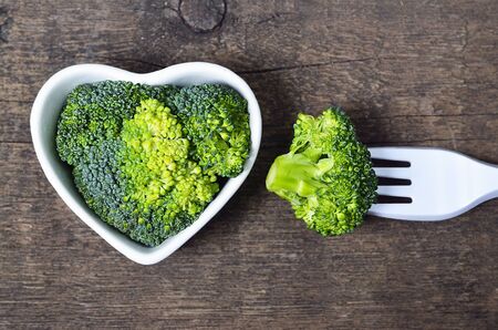 Fresh raw broccoli in a white heart shaped bowl on old wooden rustic table.Selective focus.Healthy food, raw diet or vegan food concept.の写真素材