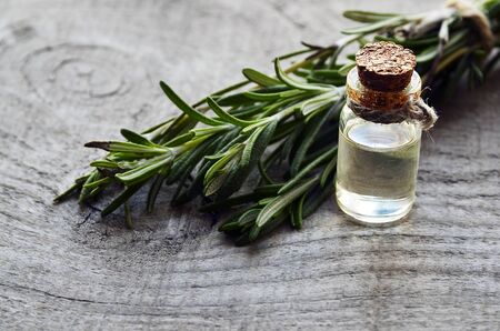Rosemary essential oil in a glass bottle with fresh green rosemary herb on old wooden table.Rosemary oil for spa, aromatherapy and bodycare.Extract oil of rosemary.Selective focus.の写真素材