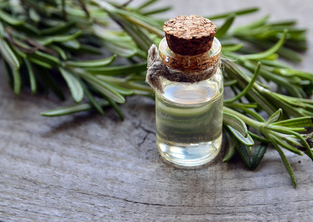 Rosemary essential oil in a glass bottle with fresh green rosemary herb on old wooden table.Rosemary oil for spa, aromatherapy and bodycare.Extract oil of rosemary.Selective focus.の写真素材