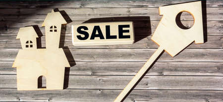 On a wooden table a block with the text sale and a homemade model of the house