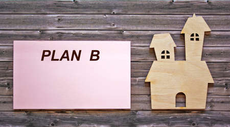 The text of plan B is written on a sticker, an icon of the house lies on a wooden tableの写真素材