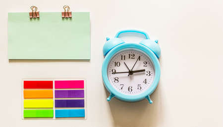 Alarm clock with blank note and colored stickers on white background.