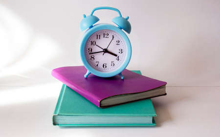 Colored notebooks and blue alarm clock on a white backgroundの写真素材