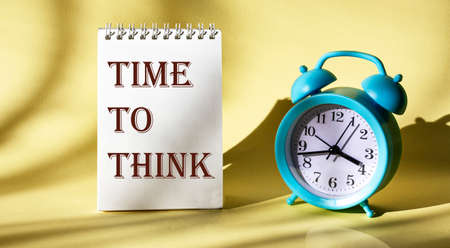 The inscription Time to think on a notepad on a light background, next to an alarm clock