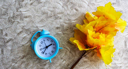Alarm clock and maple branch on the sand. Fall Season Image Style