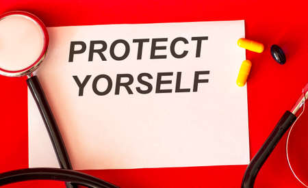 On a white sheet of paper the text protect yourself, near a stethoscope on a red backgroundの写真素材