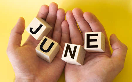 Men's hands are holding wooden blocks with the text June on a yellow backgroundの写真素材