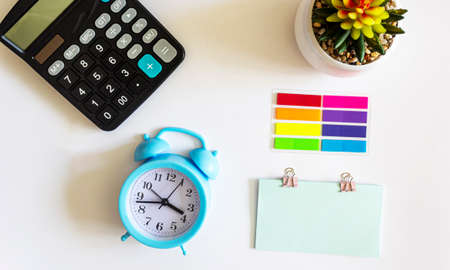 Alarm clock with stationery and flower in a pot on a white backgroundの写真素材