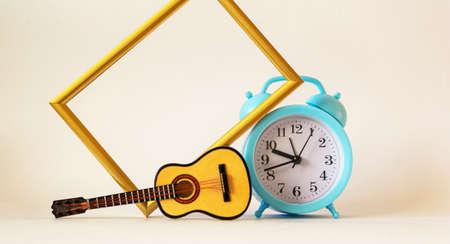 Toy guitar, blue alarm clock and gold frame on white backgroundの写真素材