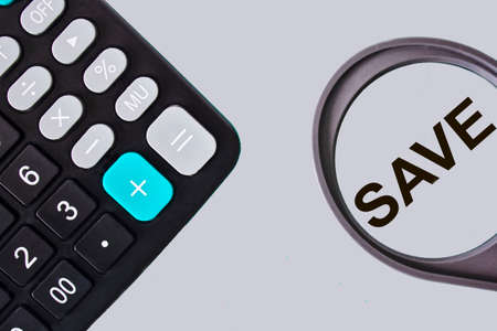 Save, text on a magnifying glass with a calculator on a light background.の写真素材