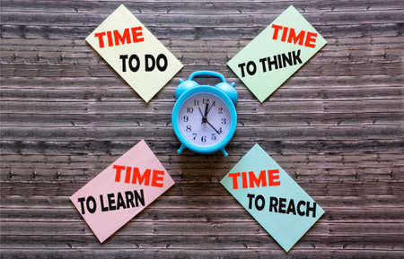Texts on stickers about time on a wooden table with an alarm clock.の写真素材